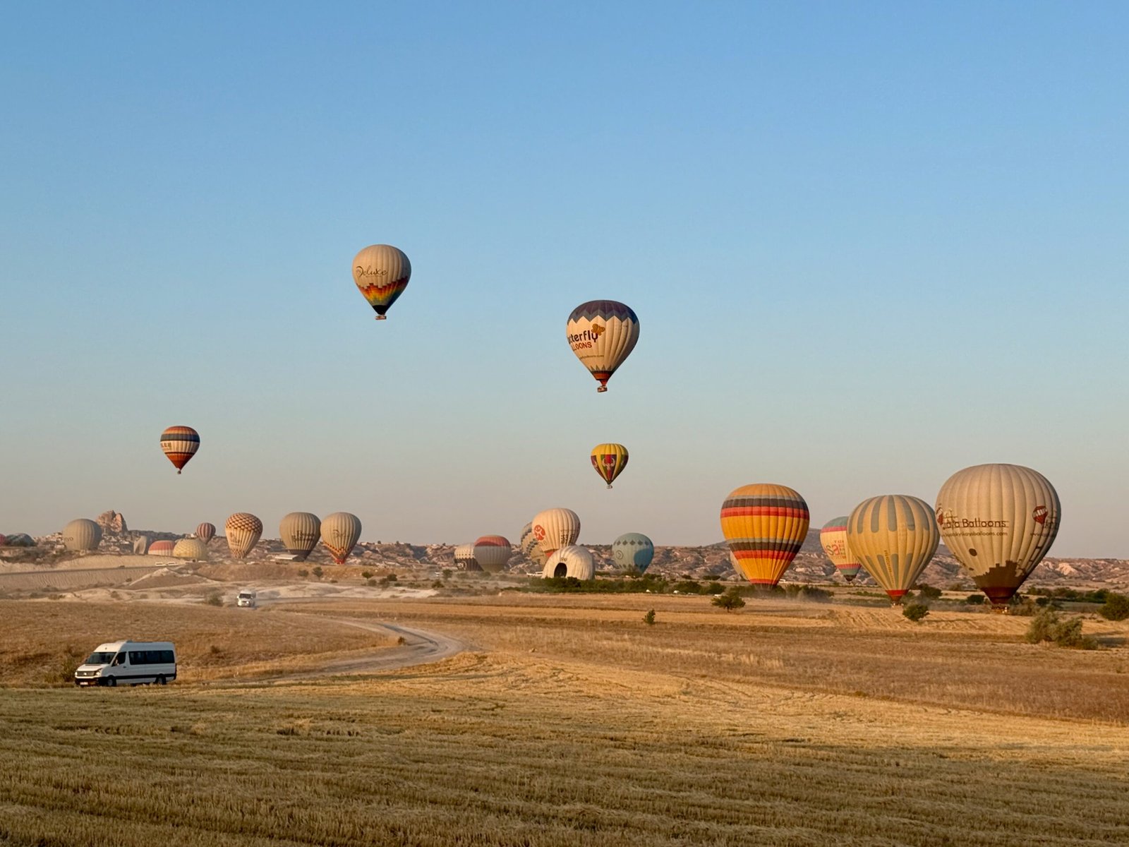 Cappadocia hot air balloons landing in a field near Göreme, Türkiye, with support vans waiting as the morning sun lights the volcanic landscape.