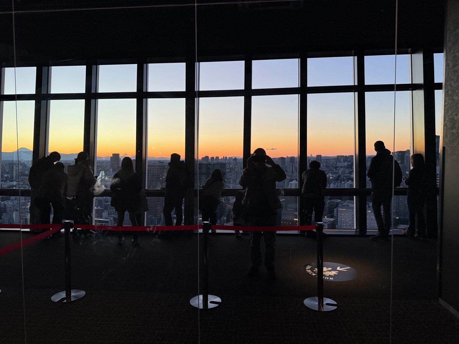 Crowd waiting at the west-facing windows of Tokyo Tower’s main deck for the Tokyo Tower sunset, with Mount Fuji visible in the far-left window panel.