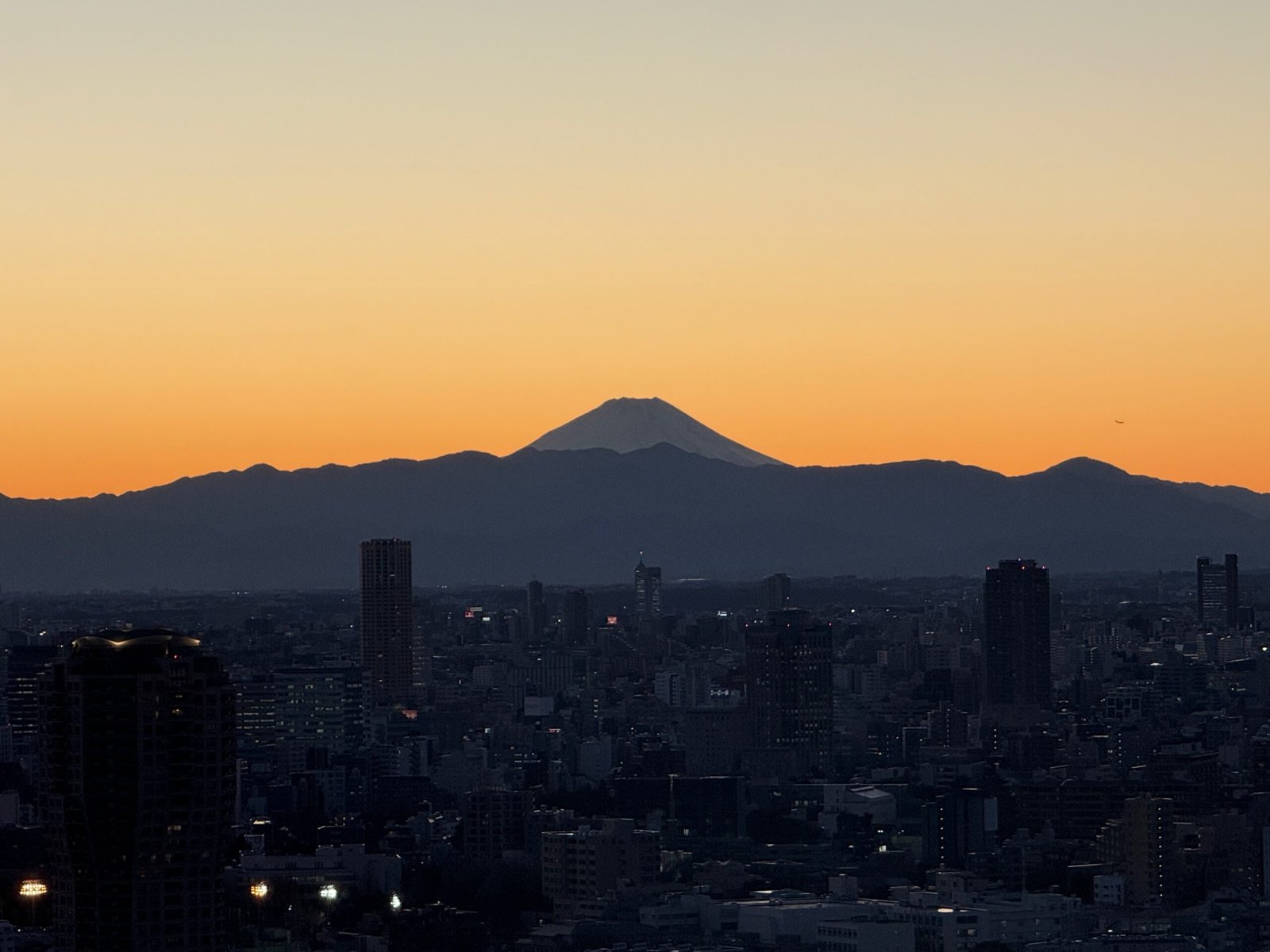Tokyo Tower sunset view of Mount Fuji silhouetted against an orange winter sky, seen from the main observation deck in Tokyo, Japan.