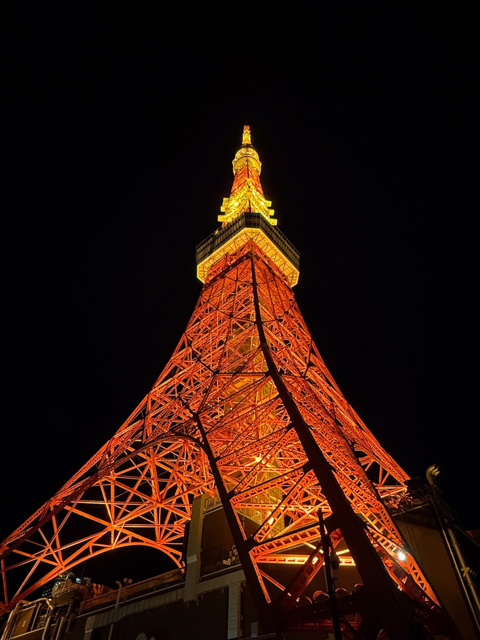 Tokyo Tower sunset photo taken after dark, showing the tower glowing in orange and yellow illumination against the night sky.