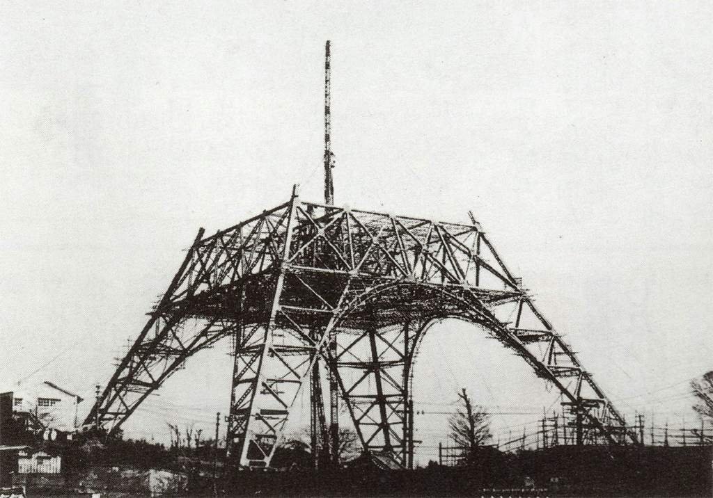 Black and white photo showing the steel frame of Tokyo Tower under construction in the 1950s, with no upper spire yet in place.