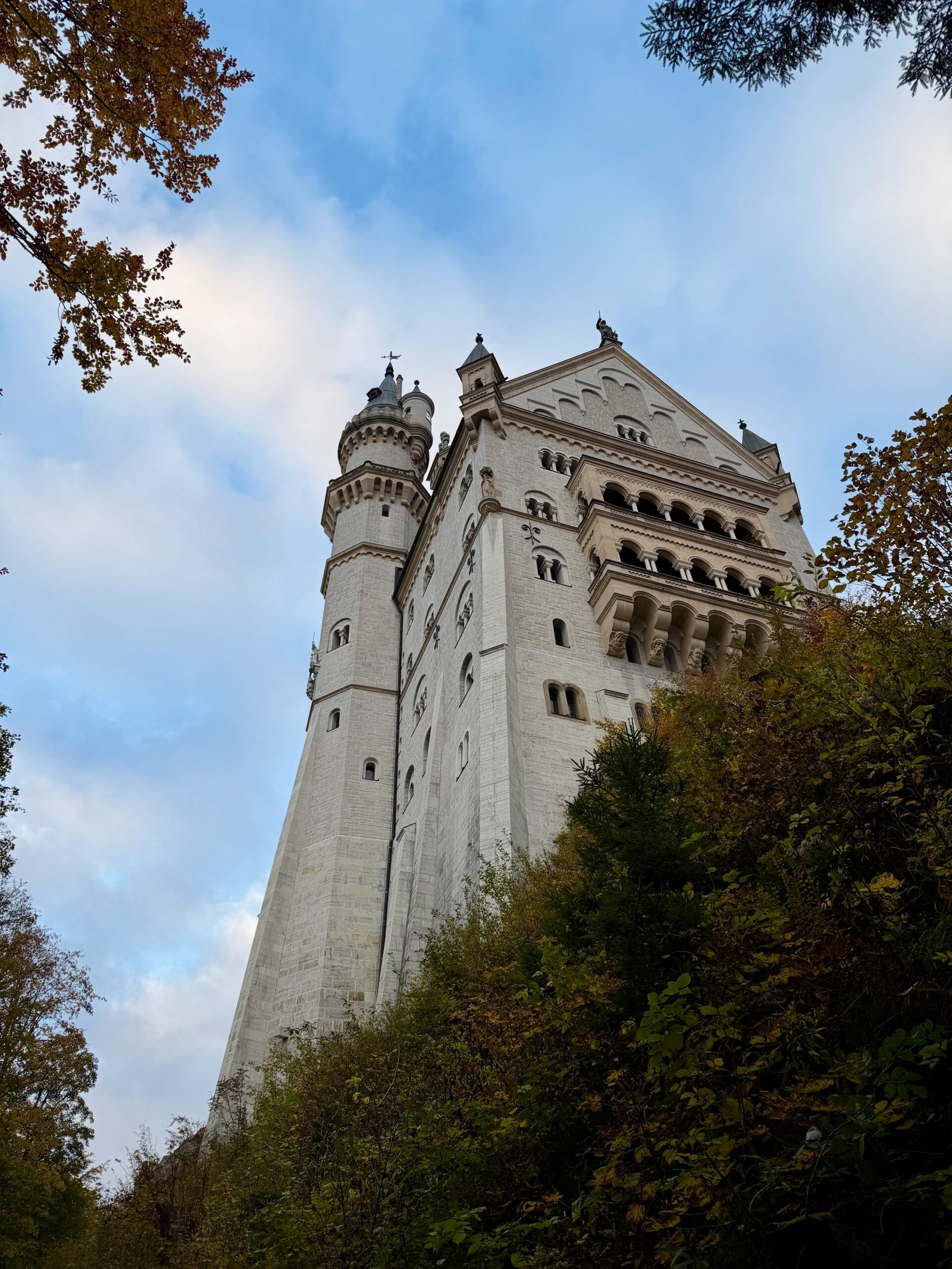 Upward view of Neuschwanstein Castle showing its Jurassic limestone walls built on a ridge above the Bavarian forest.