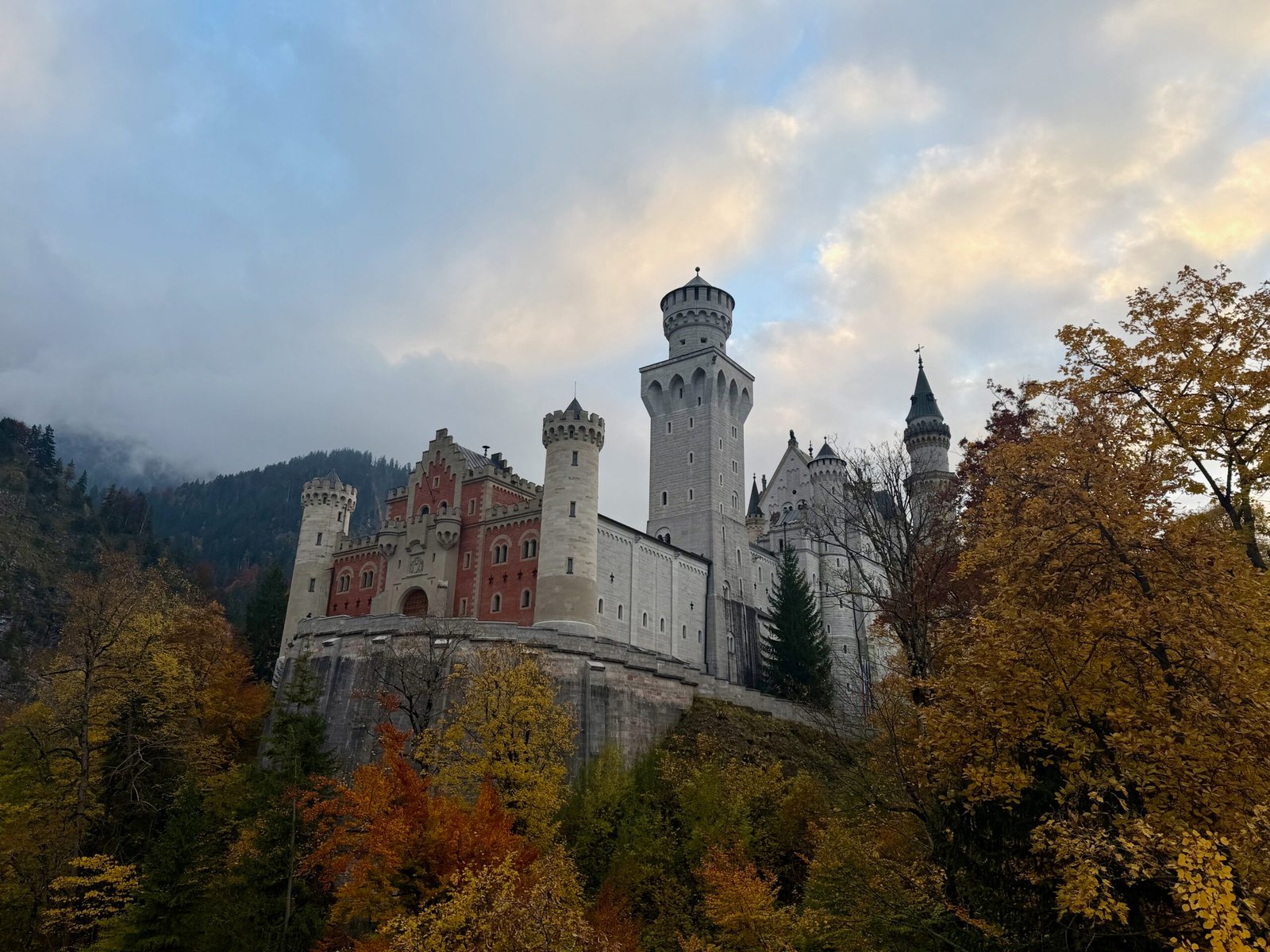 Neuschwanstein Castle at twilight surrounded by autumn forest and misty mountains in the Bavarian Alps.